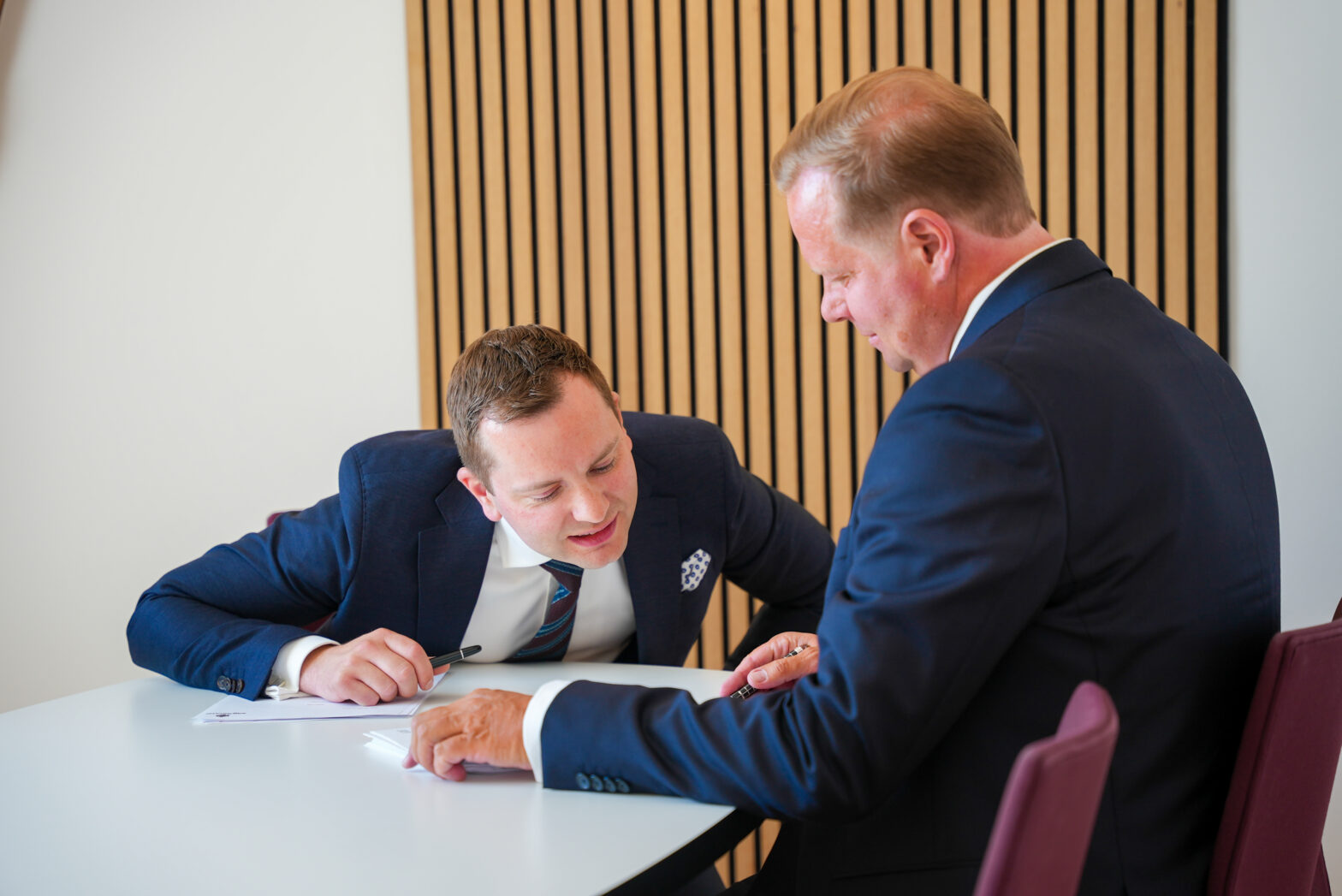 Nicklas Lund læner sig indover et bord for at læse noget på et stykke papir, der ligger foran Martin Jastram