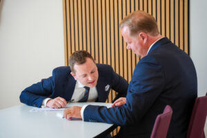 Nicklas Lund læner sig indover et bord for at læse noget på et stykke papir, der ligger foran Martin Jastram
